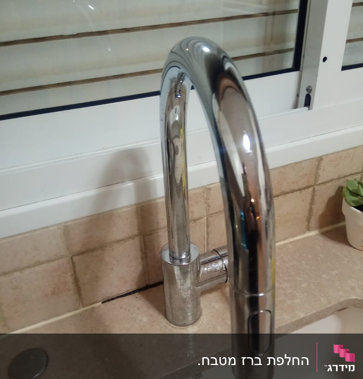 ברז מטבח כסוף על משטח שיש ליד חלון